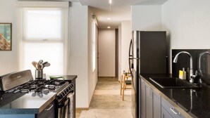 Une cuisine moderne équipée d’une cuisinière à gaz, de plans de travail noirs, d’un réfrigérateur et d’un évier.