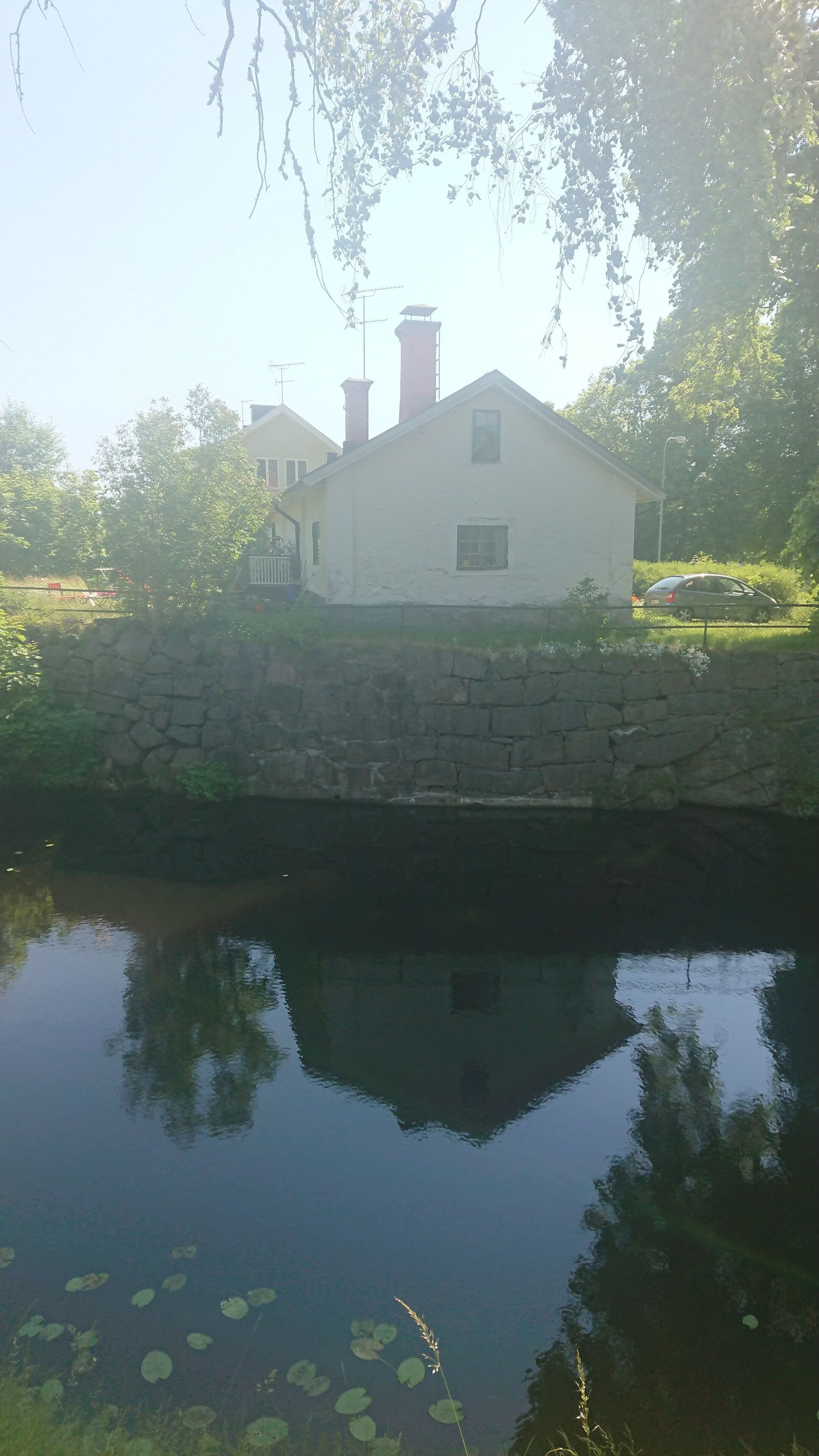 Une maison avec un mur en pierre et un étang devant.