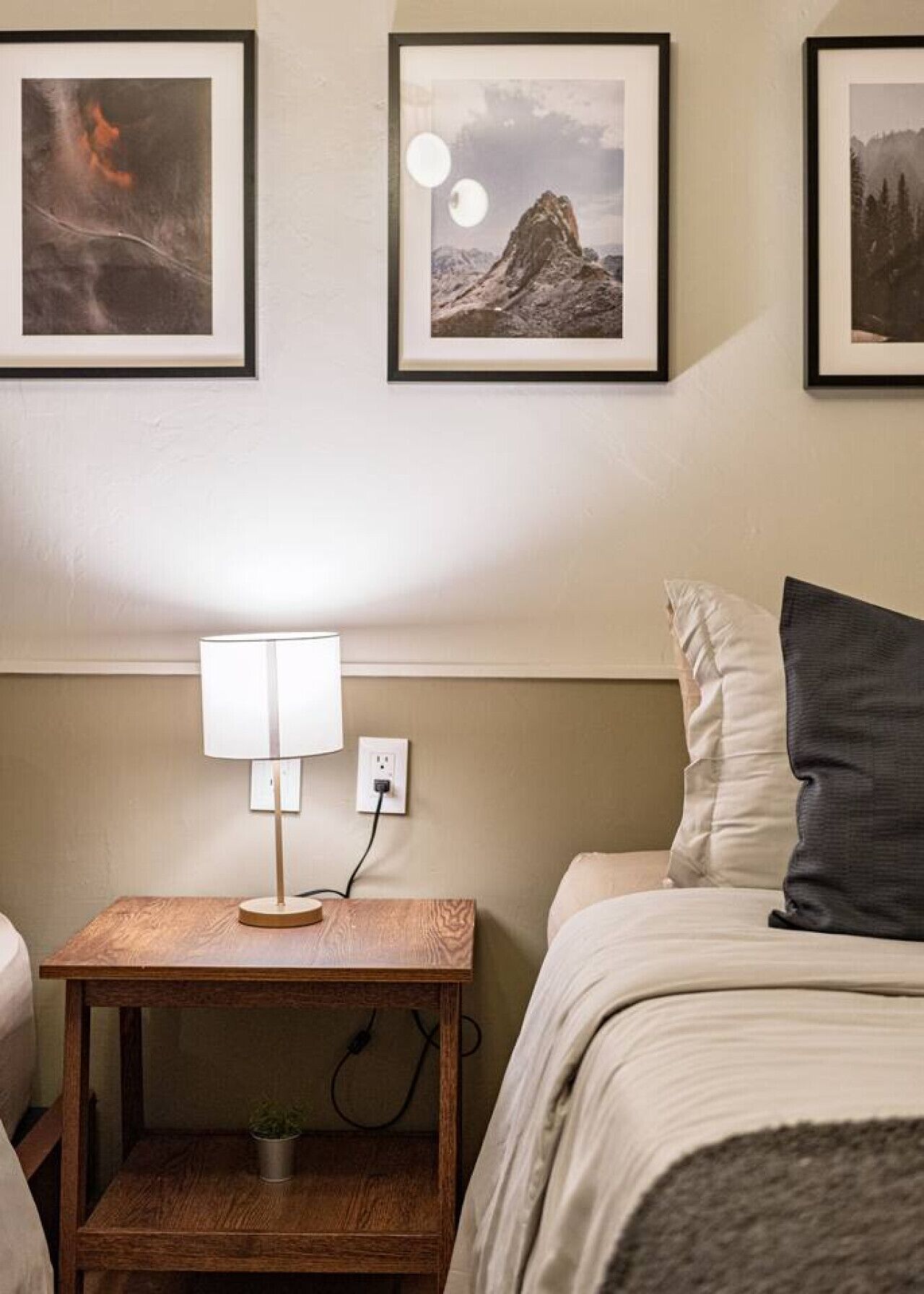 Un dormitorio con una cama, una mesita de noche con una lámpara y tres cuadros en la pared.