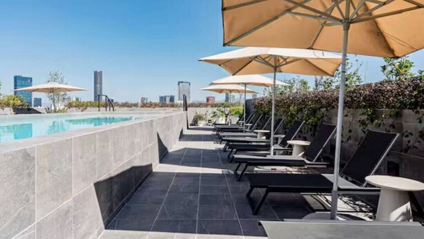 A rooftop pool area with lounge chairs and umbrellas, a clear view of the city skyline, and a modern architectural design. - Escape to Skyline Views & Rooftop Pool Bliss (Mexico City)