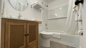 Et badeværelse med en trækommode, toilet, badekar og bruser.
