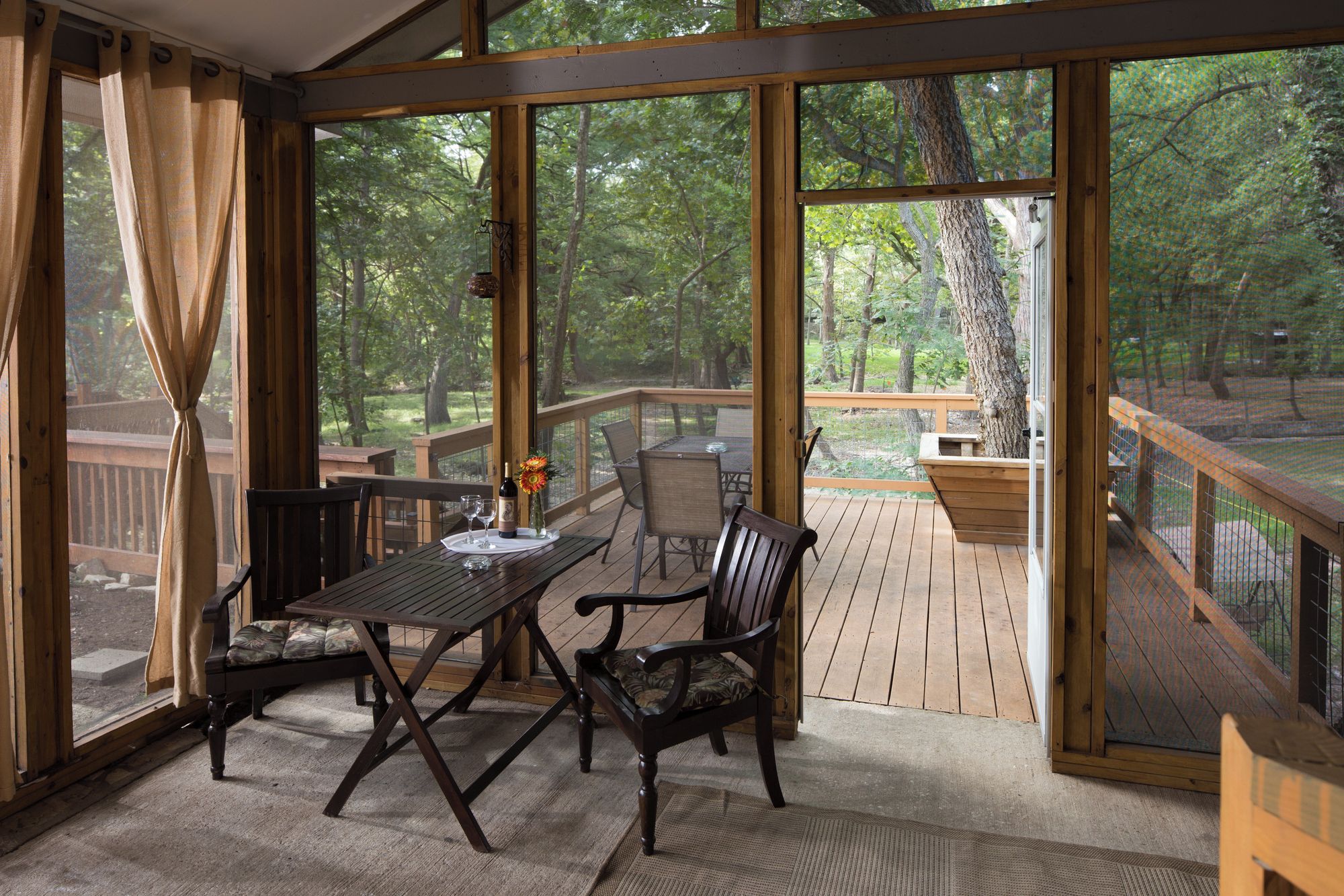 A covered outdoor seating area with a table and chairs, overlooking a wooded area.