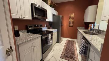 A modern kitchen with white cabinets, stainless steel appliances, and a marble floor.
