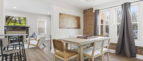 A modern dining area with a wooden table and chairs, a fireplace, and a large window with curtains.