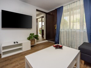 A modern living room with a flat-screen TV, a white coffee table, a dark sofa, and a large window with blue curtains. - CIRO CH / HR-07098-04 by Interhome (Selce)