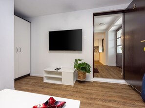 A modern living room with a flat-screen TV mounted on the wall, a white entertainment unit, a wooden floor, and a door leading to another room. - CIRO CH / HR-07098-04 by Interhome (Selce)