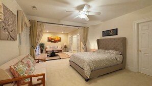 A bedroom with a large bed, a sofa, a coffee table, and a ceiling fan.