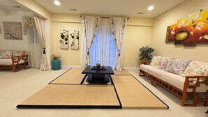 A traditional Japanese-style living room with tatami mats, a low table with a tea set, a sofa with patterned cushions, and a large painting on the wall.