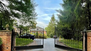 A gated driveway leading to a building with a brick wall on one side and a metal gate.
