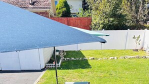 Eine Terrasse im Freien mit Tisch und vier Stühlen, einem blauen Sonnenschirm und einem gemusterten Teppich.