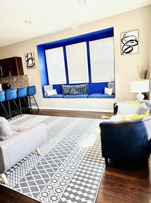 Ein Wohnzimmer mit blauer Akzentwand, einem gemusterten Teppich und einer Sitzecke mit Sofa und Sesseln.