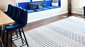 Ein modernes Wohnzimmer mit blauer Akzentwand, einer Sitzecke mit Sofa und Sesseln, einem Esstisch und einem gemusterten Teppich.