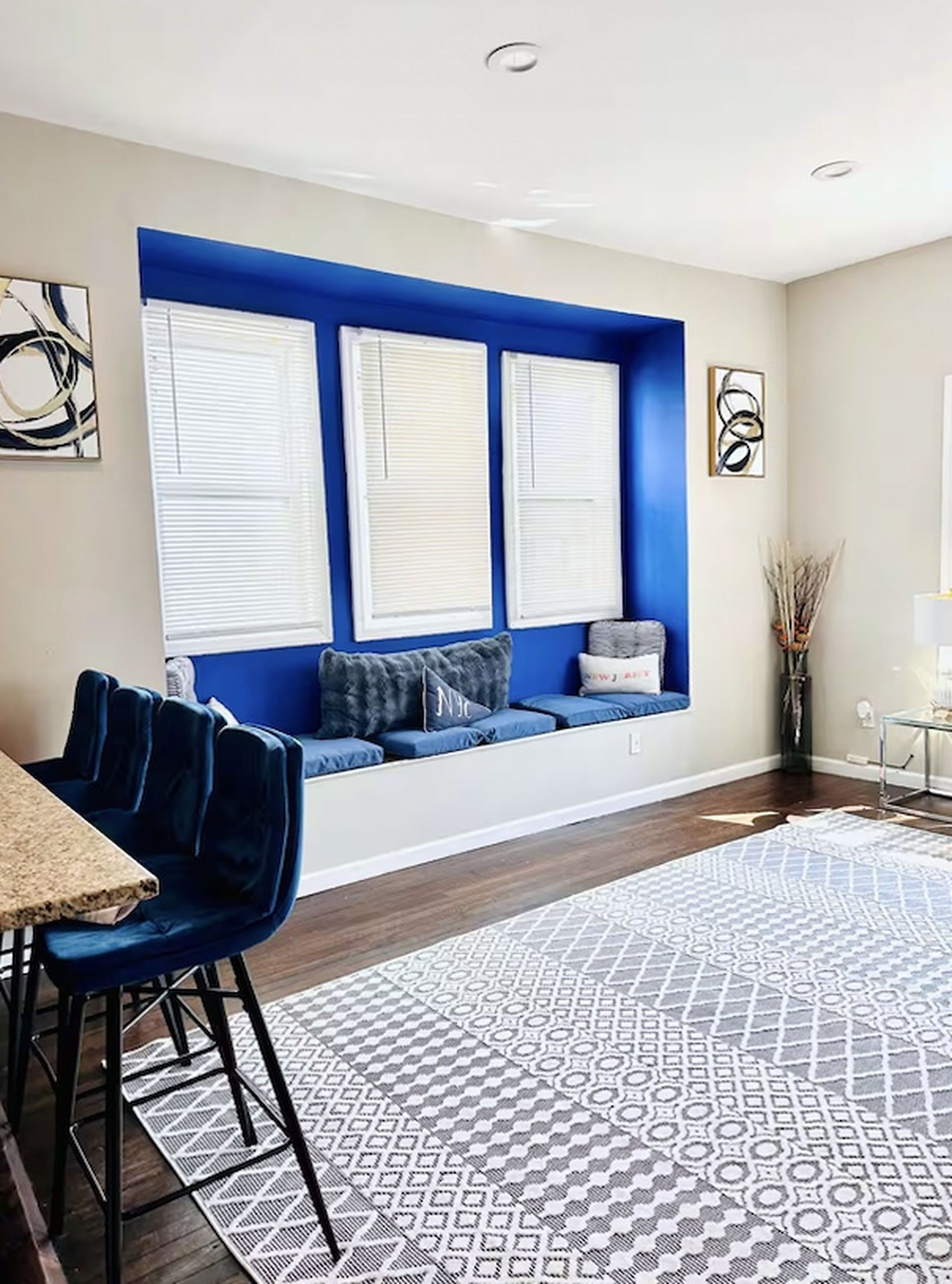 A modern living room with a blue accent wall, a seating area with cushions, a patterned rug, and a dining area with a table and chairs.