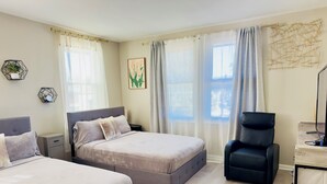 Ein Hotelzimmer mit zwei Betten, einem Schreibtisch mit Stuhl und einem großen Fenster mit Vorhängen.