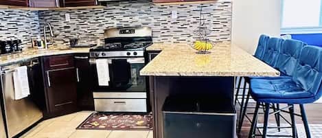 Una cocina moderna con armarios de madera oscura, un microondas de acero inoxidable, una estufa a gas y una pequeña isla con un cubo de basura.