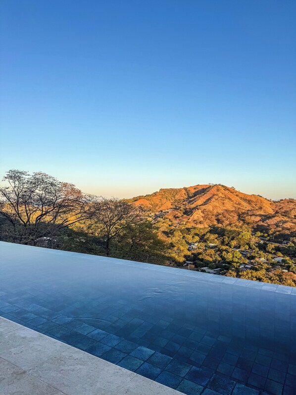 An infinity pool with a view of a mountainous landscape and trees.