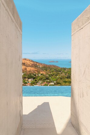 A view from a balcony overlooking a coastal area with a clear sky, a body of water, and distant landforms. - VISTA PACIFICO (Coco)