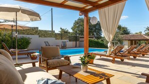 Un'area esterna coperta con piscina, lettini e un tavolo.
