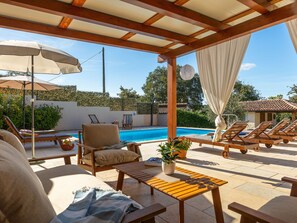 Un espacio al aire libre techado con piscina, sillas de descanso y una mesa.