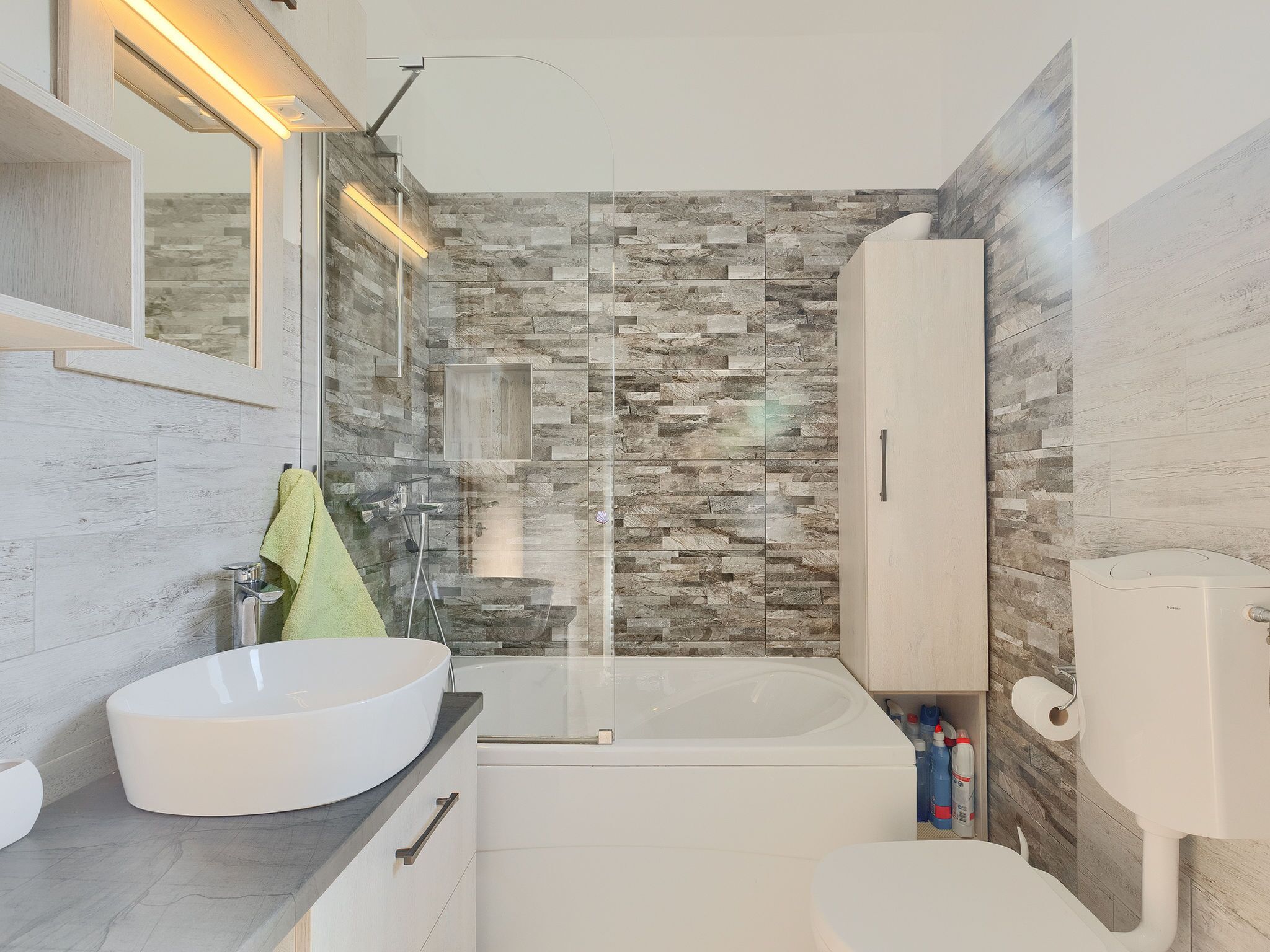Un baño moderno con pared de piedra, lavamanos blanco, bañera y retrete.