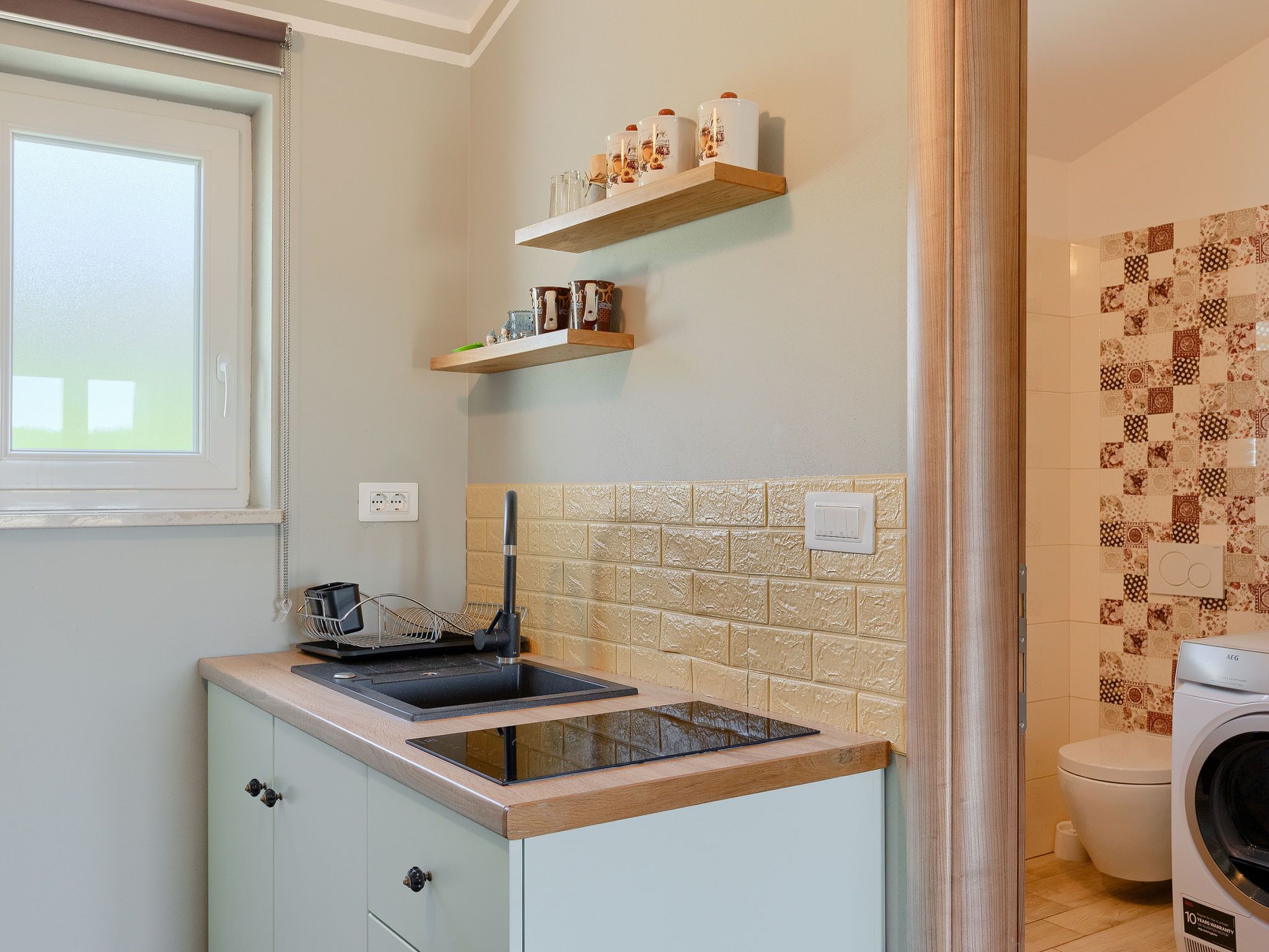 A kitchen with a built-in sink, a window, and a washing machine in the adjacent bathroom.