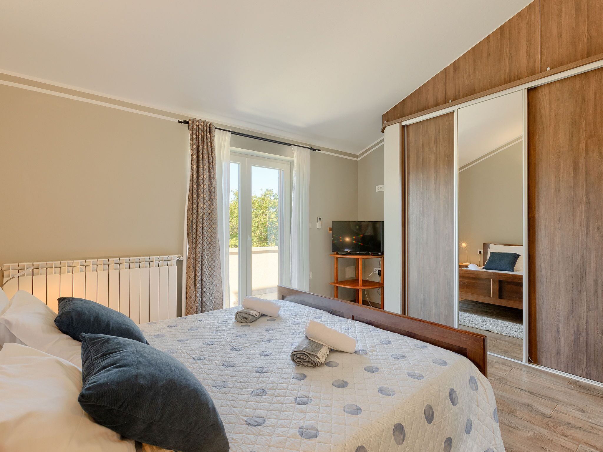 Une chambre à coucher comprenant un lit, une télévision, une armoire et une porte coulissante donnant sur un balcon.