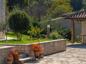 Un patio con muro de piedra, plantas en macetas y una estructura de techo de tejas.