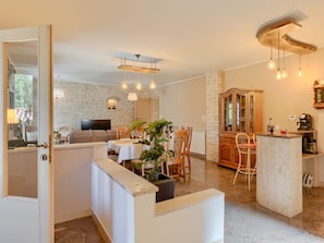Un comedor espacioso con un muro de piedra de fondo, una televisión y un mueble de madera con puertas de cristal.