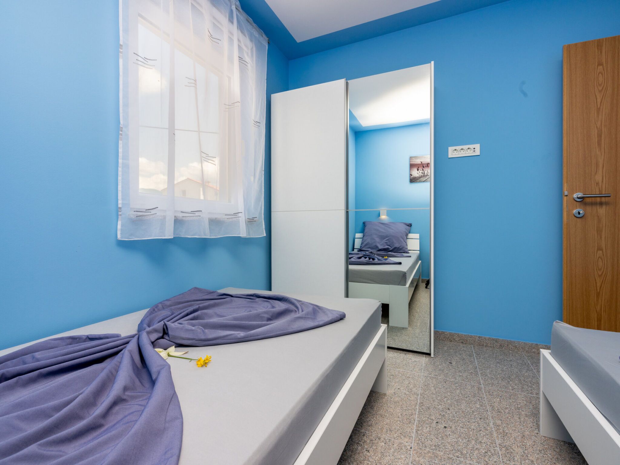 Une chambre avec un lit simple, une porte en bois et une fenêtre ornée de rideaux légers.