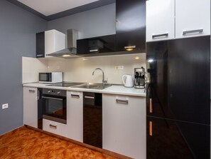 Cocina compacta con microondas, estufa, lavamanos y refrigerador negro.
