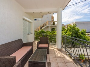 Ein Balkon mit Korbmöbeln, einem Glastisch und einem Metallgeländer.