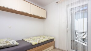 Una habitación pequeña y moderna con una cama, una mesa de madera y un ventanal corredero que da a un balcón exterior.