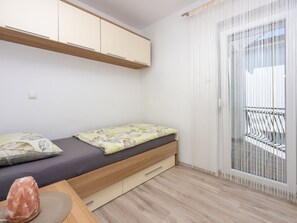 Ein kleiner, moderner Raum mit einem Bett, einem Holztisch und einer Glastür, die auf einen Balkon im Freien führt.