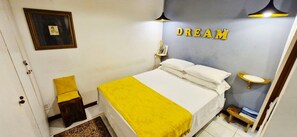 A bedroom with a bed, a bedside table, a nightstand, a lamp, and a wall with the word "DREAM" spelled out in letters. - COPSE0101 - Edifício Themis (Salvador)