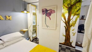 Een slaapkamer met een bed, een wandlamp, een spiegel en een schilderij van een boom.
