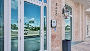 A hotel entrance with a glass door, a marble pillar with the number 3420, a security keypad, and a trash bin. - Miami Beach Studio Quiet Oasis (Miami Beach)