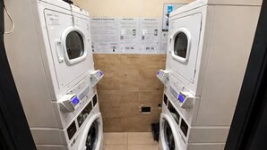 A laundry room with two stacked washing machines, a tiled wall with informational posters, and a drain in the floor. - Miami Beach Studio Quiet Oasis (Miami Beach)