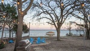 Un barbecue, des chaises bleues et un kiosque au bord d’un lac.