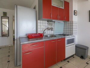 Een keuken met rode kastjes, een roestvrijstalen spoelbak, een gasfornuis en een prullenbak.