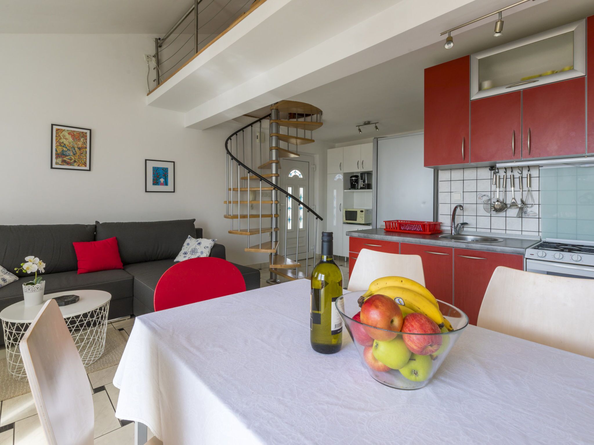 Una cocina moderna con armarios rojos, un comedor con mesa dispuesta para dos personas y una escalera que sube a un nivel superior.