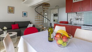 A modern kitchen with red cabinets, a dining area with a table set for two, and a staircase leading to an upper level. - STIVIC 2 / HR-08046-01 by Interhome (Selce)