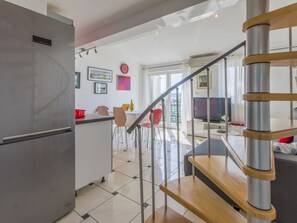 Eine moderne Küche mit einem Edelstahlkühlschrank, ein Essbereich mit Tisch und Stühlen sowie eine Treppe, die in einen Wohnbereich mit einem Fernseher führt.