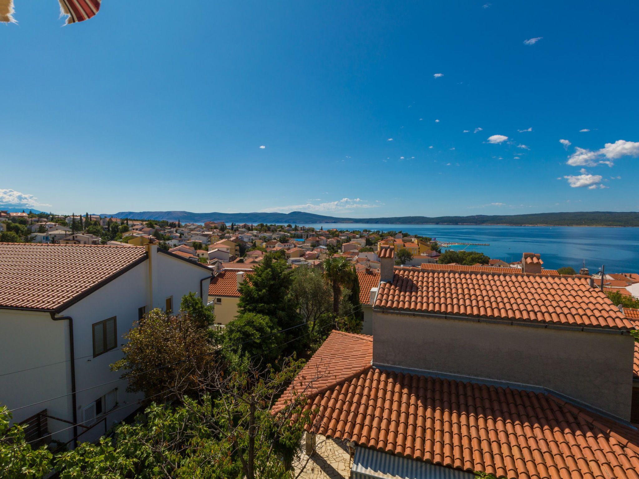 A coastal town with terracotta-roofed buildings, a clear blue sky, and a view of the sea.