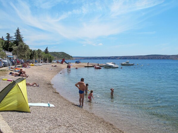 Uma praia com uma tenda, pessoas relaxando e barcos na água.