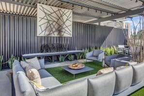 A modern outdoor patio with a sectional sofa, a dining table, and a large abstract wall art piece. - New Luxury Condo with Dual Primary Bedrooms + 1/2 bath. Resort style heated pool (Palm Springs)