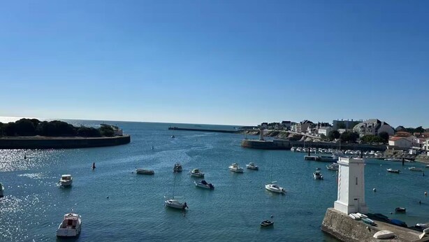 Une ville côtière dotée d’un port de plaisance rempli de bateaux, d’un phare et de bâtiments qui bordent le front de mer.