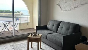 Un balcon avec un canapé gris, une petite table en bois et une vue sur la mer.