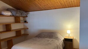 Une chambre à coucher avec un lit, des étagères en bois, une table de chevet avec une lampe et un plafond en pente.