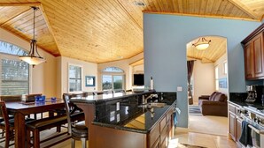 Una cocina amplia con una isla grande, techo de madera y vista al área de estar.