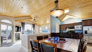 Un comedor amplio con una gran mesa y sillas de madera, una cocina con armarios oscuros y vistas amplias a través de grandes ventanas.